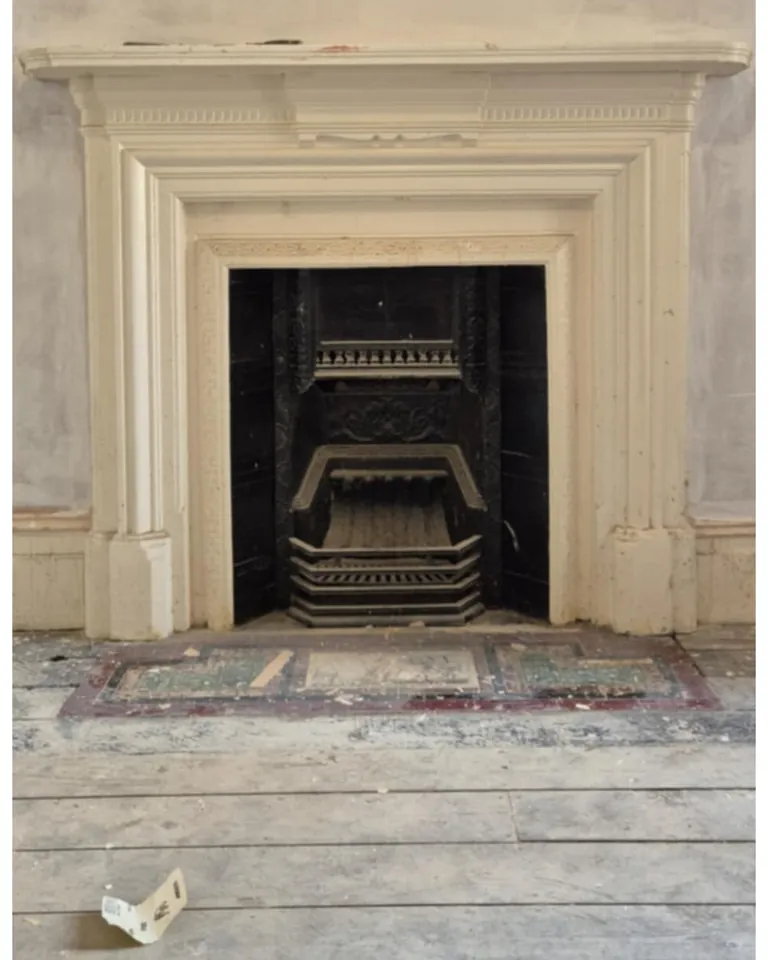 A cast-iron fireplace before, painted over in white