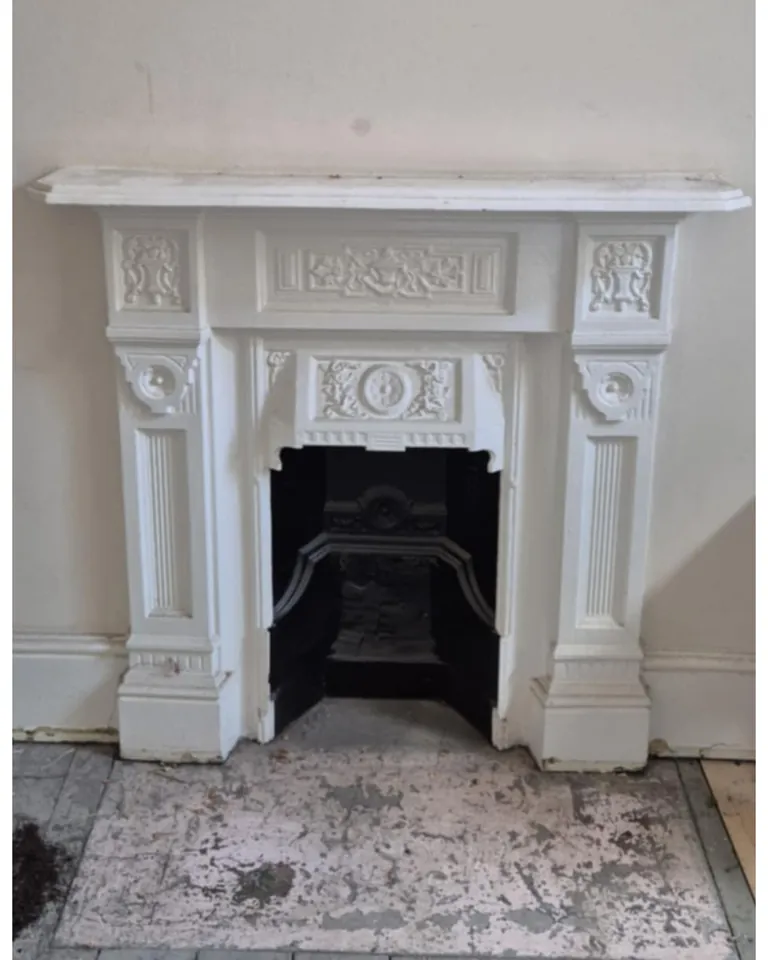 An ornate cast-iron fireplace before, painted white